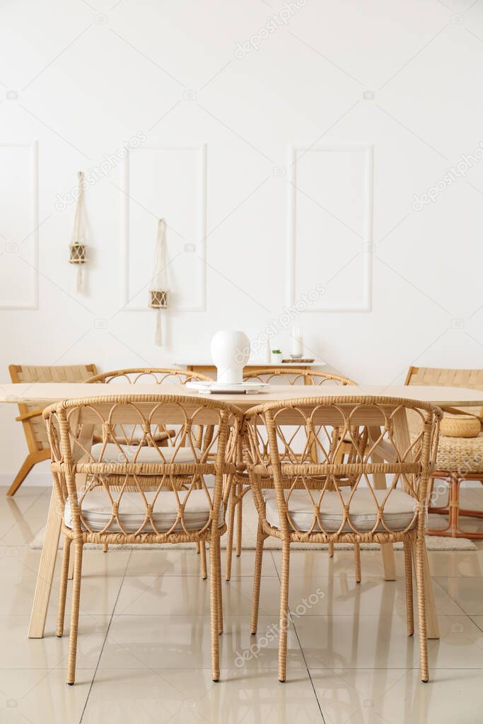 Wooden table with wicker chairs in interior of light dining room