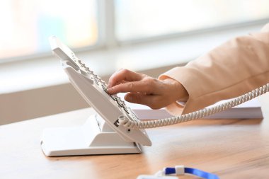 Olgun sekreter ofisteki telefon numarasını arıyor, kapatıyor.