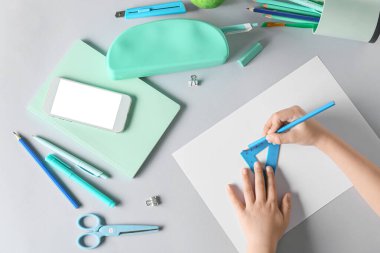 Beyaz arka planda kırtasiye malzemesi ve cep telefonu olan çocuk elleri