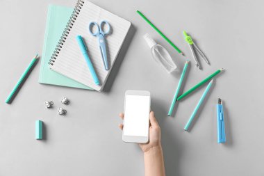 Beyaz arka planda cep telefonu, bir şişe dezenfektan ve kırtasiye malzemesi olan bir çocuk eli.