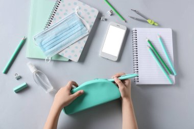 Kalem kutusu, tıbbi maske, cep telefonu ve beyaz arka planda kırtasiye malzemesi olan çocuk elleri