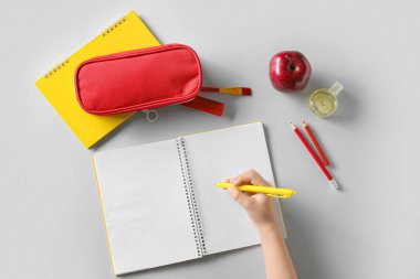 Kalemle çocuk eli, boş defter, beyaz arka planda bir şişe dezenfektan, elma ve kırtasiye malzemesi.