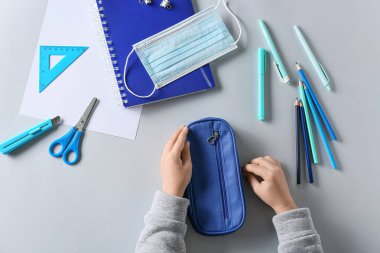 Beyaz arka planda çocuk elleri kalem kutusu, kırtasiye ve tıbbi maske