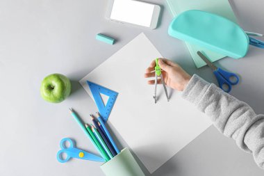 Beyaz zemin üzerinde farklı kırtasiye malzemesi, elma ve cep telefonu olan çocuk eli