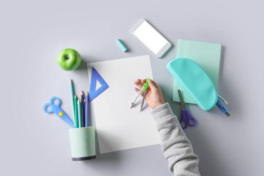 Beyaz arkaplanda kırtasiye malzemesi ve cep telefonu olan çocuk eli