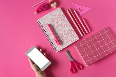 Pembe arka planda cep telefonu ve farklı kırtasiye malzemesi olan çocuk eli