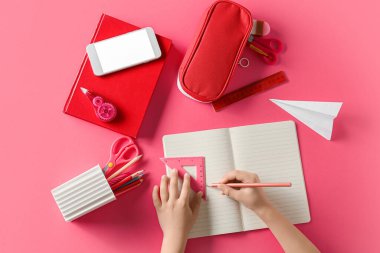 Pembe arka planda kırtasiye malzemesi ve cep telefonu olan çocuk elleri