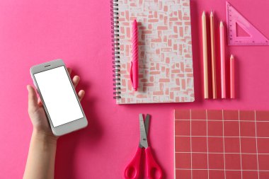 Pembe arka planda cep telefonu ve farklı kırtasiye malzemesi olan çocuk eli