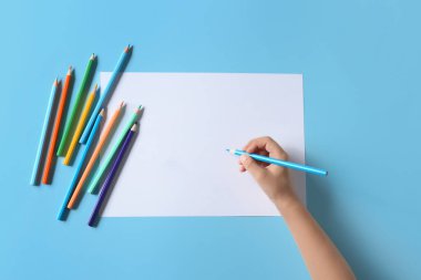 Boş kağıt ve farklı renk arkaplanlı farklı kalemlerle çocuk eli