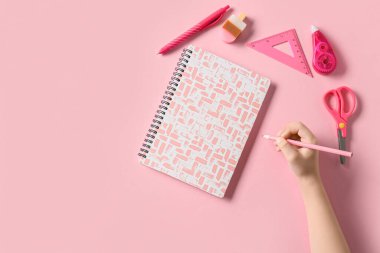 Pembe arka planda farklı kırtasiye malzemesi olan çocuk eli