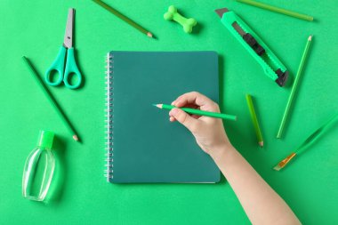 Kırtasiye malzemesi ve yeşil arka planda bir şişe dezenfektanla çocuk eli.