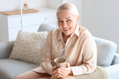 Kanepede otururken sıcak çay içen olgun bir kadın.