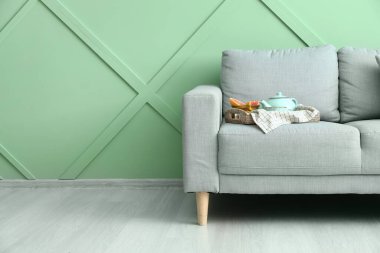 Yeşil duvarın yanındaki şık kanepede çaydanlıklı tepsi.