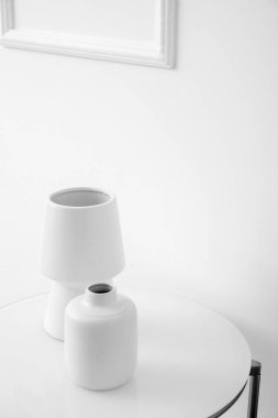 Beyaz vazolar ışık duvarının yanındaki masada.