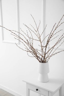 Işık duvarının yanındaki beyaz masada ağaç dalları olan vazo.