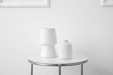 Beyaz vazolar ışık duvarının yanındaki masada.