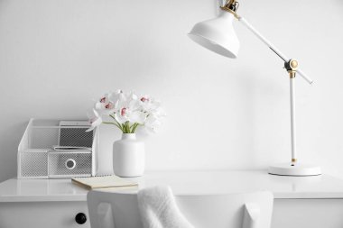 Tablet bilgisayarı, çiçekleri ve lambası olan organizatör beyaz duvarın yanında.