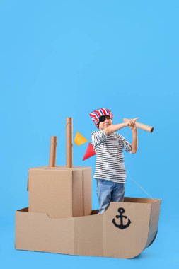 Mavi arka planda karton gemiyle oynayan sevimli küçük çocuk.