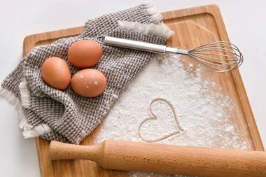 Tahta tahta tahta tahta, tavuk yumurtası, un, çizilmiş kalp ve hafif arka planda çırpma.