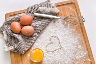 Tahta tahta tahta tahta, tavuk yumurtası, un, çizilmiş kalp ve hafif arka planda çırpma.