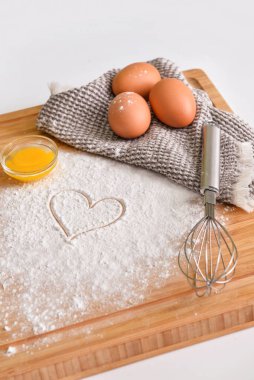 Tahta tahta tahta tahta, tavuk yumurtası, un, çizilmiş kalp ve hafif arka planda çırpma.