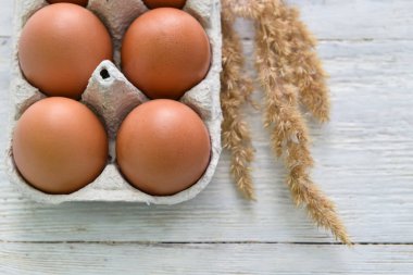 Beyaz ahşap arka planda taze tavuk yumurtası ve dikenli tutucu, yakın plan.