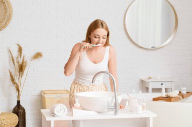 Güzel olgun bir kadın banyoda dişlerini fırçalıyor.