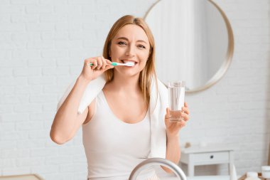 Güzel olgun bir kadın banyoda dişlerini fırçalıyor.