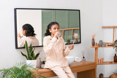 Banyoda dişlerini fırçaladıktan sonra bir bardak suyla gezen Afro-Amerikalı genç kız.