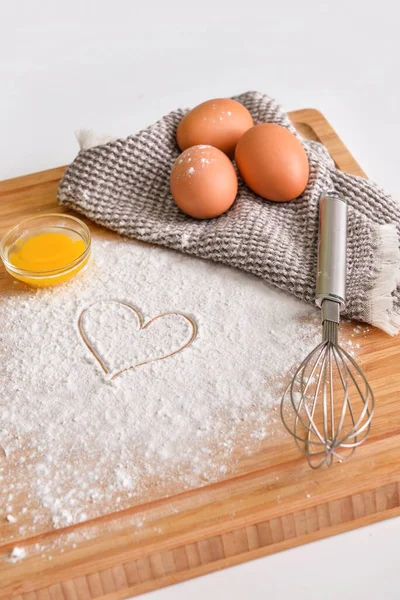 Tahta tahta tahta tahta, tavuk yumurtası, un, çizilmiş kalp ve hafif arka planda çırpma.