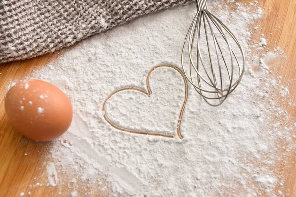 Taze tavuk yumurtası, kalbi çizilmiş un ve ahşap arka planda çırpma.