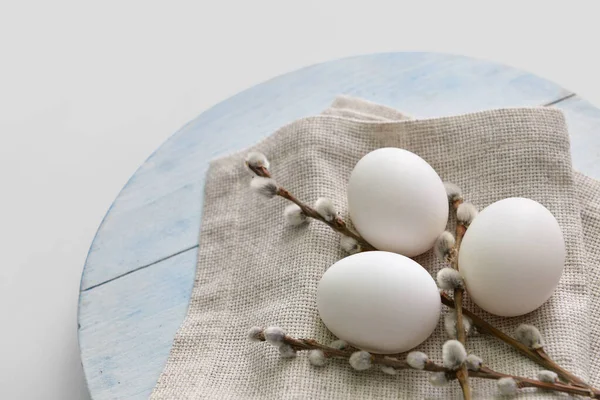 Wooden board with fresh chicken eggs and pussy willow branches on light background, closeup