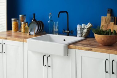 Mutfak aletleriyle seramik lavabo ve mavi duvarın yanındaki tezgahlarda yiyecek.