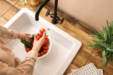 Bej duvarın yanındaki lavaboda taze sebze yıkayan kadın.