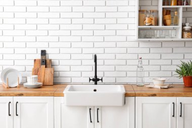 Lavabo ve mutfak gereçleri beyaz tuğla duvarın yanında.