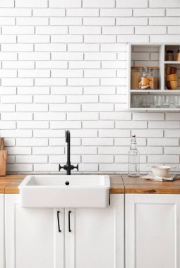 Lavabo ve mutfak gereçleri beyaz tuğla duvarın yanında.