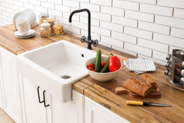 Seramik lavabo, sebzeli kase ve beyaz tuğla duvarın yanındaki tezgahlarda ekmek.