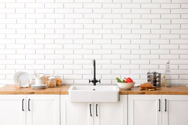 Lavabo, yemek ve mutfak gereçleri beyaz tuğla duvarın yanında.