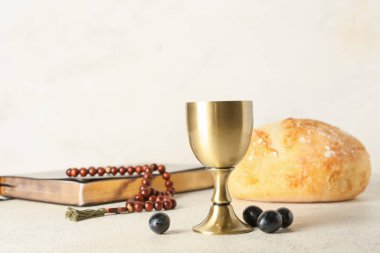 Kutsal İncil 'li bir bardak şarap, arka planda tespih ve ekmek.