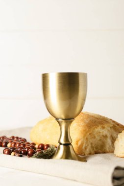 Beyaz ahşap zemin üzerinde ekmek ve tespih bulunan bir bardak şarap.