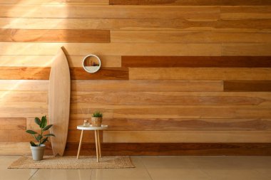 Sörf tahtası ve masa, ahşap duvarın yanında bitkiler.