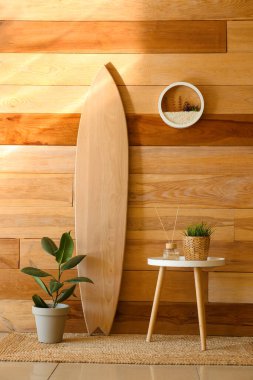 Sörf tahtası ve masa, ahşap duvarın yanında bitkiler.
