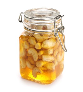 Beyaz arka planda ballı bir kavanoz lezzetli kaju fıstığı.