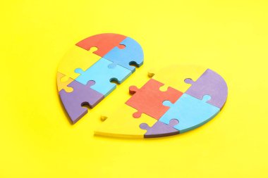 Sarı arka planda renkli yapboz parçalarından yapılmış bir kalp. Otistik bozukluk kavramı