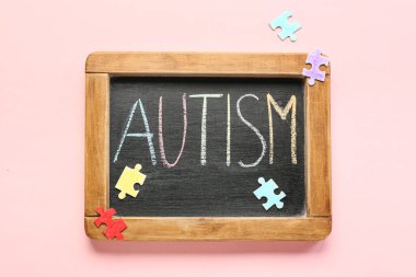 Pembe arka planda kelime AUTISM ve yapboz parçaları ile tebeşir tahtası