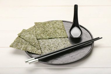 Hafif ahşap zemin üzerinde lezzetli deniz yosunları, yemek çubukları ve soya sosu tabağı