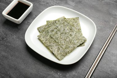 Soya soslu lezzetli deniz yosunları tabağı ve siyah arka planda çubuklar.