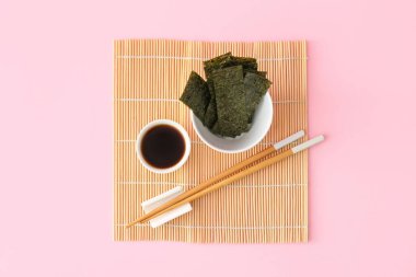 Bir kase lezzetli yosun çarşafları, yemek çubukları ve pembe arka planda soya soslu kase.