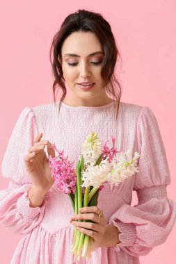 Pembe arka planda sümbül çiçekleri olan güzel genç bir kadın.