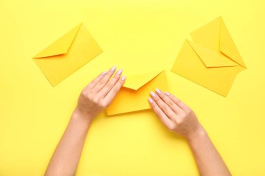 Sarı arka planda güzel manikürlü ve zarflı kadın elleri.